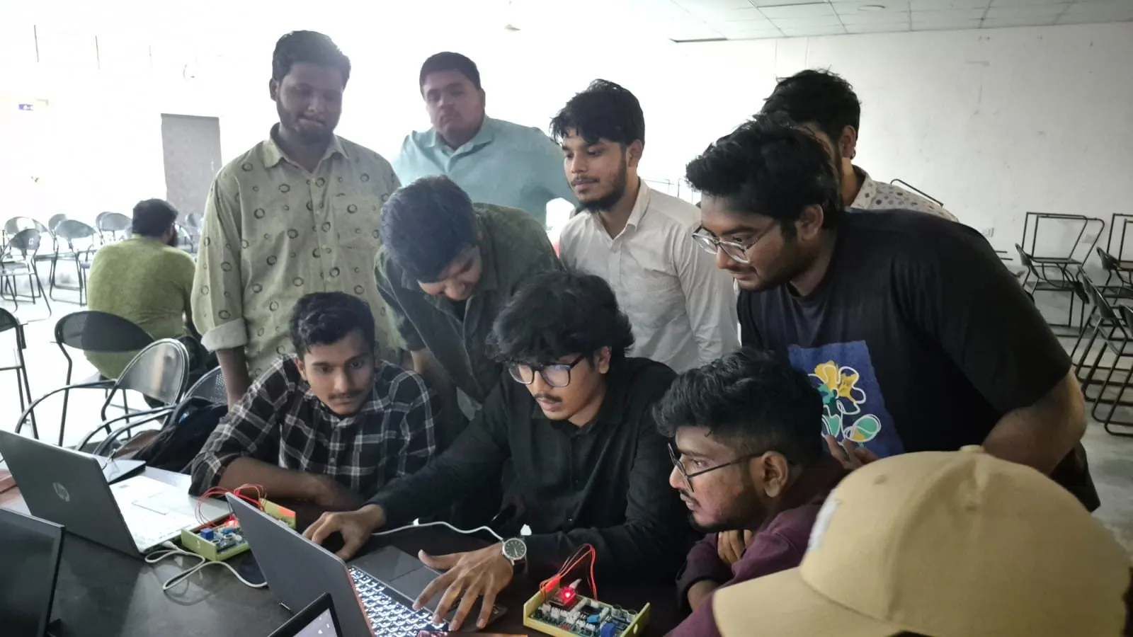 Students gathered around laptops and trainer boards during an IoT session