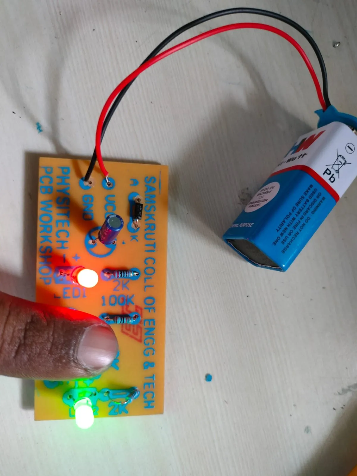 A finished PCB powered by a battery with its LED glowing